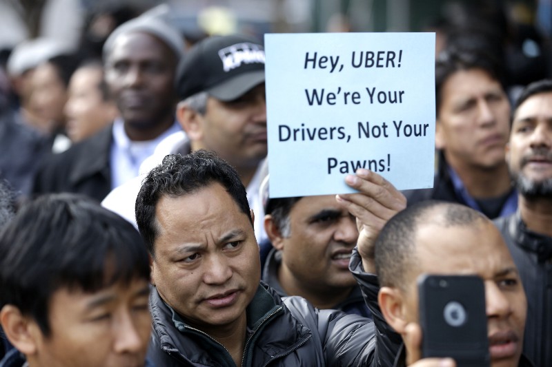 Uber drivers and their supporters hold signs during a rally at an Uber office in New York on February 1, 2016, following a 15 percent fare cut. CREDIT: AP PHOTO/SETH WENIG