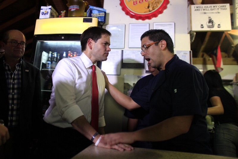 Republican presidential candidate, Sen. Marco Rubio, R-Fla., left center, listens to a supporter at a restaurant in the Santurce district of San Juan, Puerto Rico, Friday, Sept. 4, 2015. The U.S. territory must find its own way to get its financial house in order, Rubio wrote in an op-ed published in Spanish Friday in El Nuevo Dia, Puerto Rico’s largest newspaper. The Florida Republican opposes efforts to allow Puerto Rico to use bankruptcy laws to deal with a staggering $72 billion debt. CREDIT: AP PHOTO/RICARDO ARDUENGO