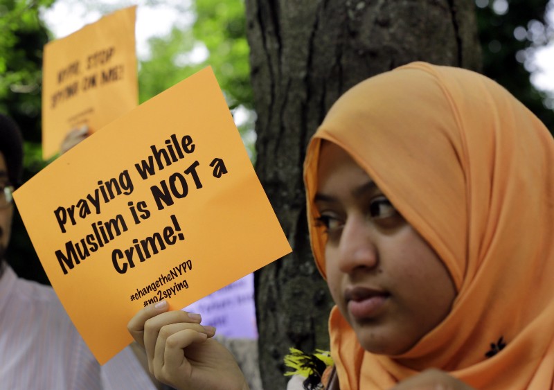 Supporters of a lawsuit challenging the NYPD’s Muslim surveillance program, hold signs during a gathering on a plaza in front of New York City Police Department headquarters, Tuesday, June 18, 2013. In a lawsuit filed Tuesday, civil rights lawyers urged a U.S. judge to declare the NYPD’s widespread spying programs directed at Muslims to be unconstitutional, order police to stop their surveillance and destroy any records in police files. CREDIT: AP PHOTO/RICHARD DREW