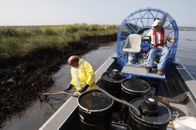 Harold Cline, in yellow, vacuums up oil that recently washed up as air boat pilot John Mouchon looks on in a cove in Barataria Bay on the coast of Louisiana, Saturday, July 31, 2010. CREDIT: AP Photo/Patrick Semansky