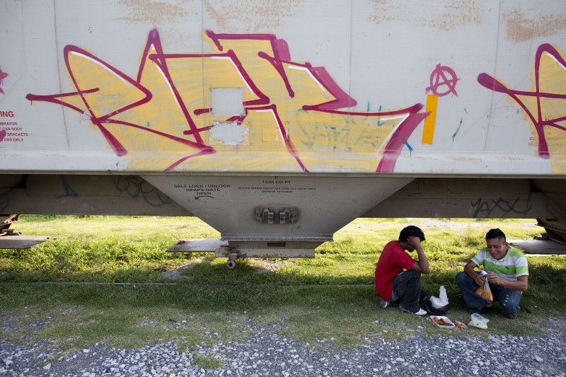In this Aug. 26, 2014, a pair of Central American migrants has lunch under a train as they wait for it to depart from Arriaga, Mexico. A Mexican crackdown seems to be keeping women and children off the deadly train, known as “The Beast,” that has traditionally helped thousands of migrants head north. The city, once bustling with migrants waiting to board the train, emptied out almost overnight. (AP Photo/Rebecca Blackwell) CREDIT: AP PHOTO/REBECCA BLACKWELL