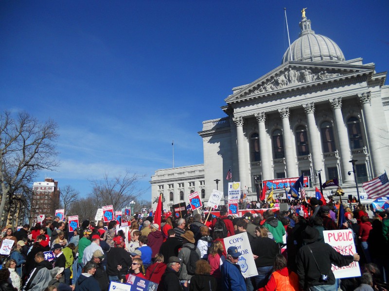 People stand in front of the Capital in Madison, Wis. on Saturday, March 10, 2012. Wisconsin unions are gathering for a rally to mark the one-year anniversary of the state Legislature passing a bill to end collective bargaining rights for most public workers in the state. CREDIT: AP PHOTO/BARBARA RODRIGUEZ