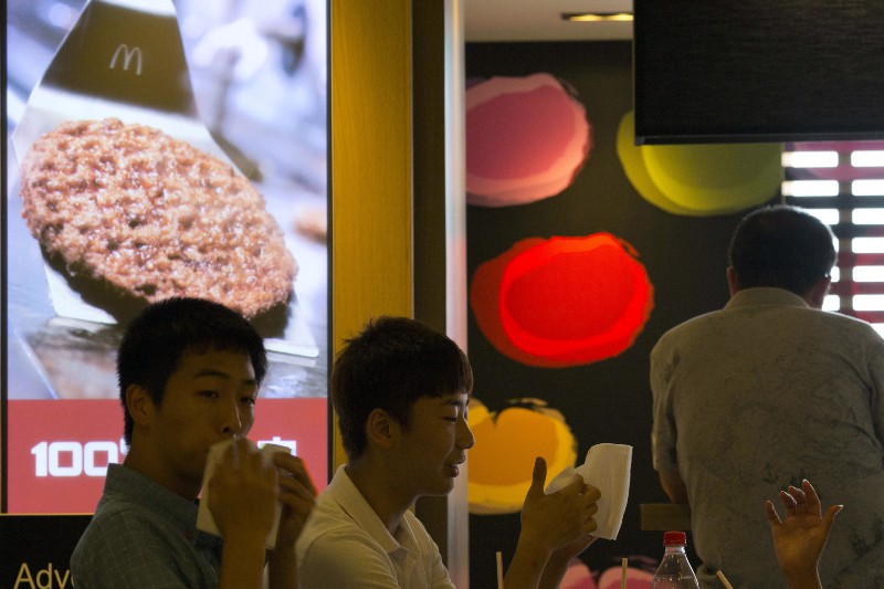 Customers enjoy their meal near an advertisement claiming to use 100 percent beef at a McDonald’s restaurant in Beijing Tuesday, July 22, 2014. CREDIT: AP PHOTO/NG HAN GUAN