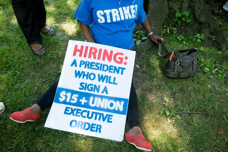 A federal contract worker sits under a tree following a march past the Capitol to a rally on Capitol Hill in Washington, Wednesday, July 22, 2015, to push for a raise to the minimum wage to $15 an hour. CREDIT: AP Photo/Andrew Harnik