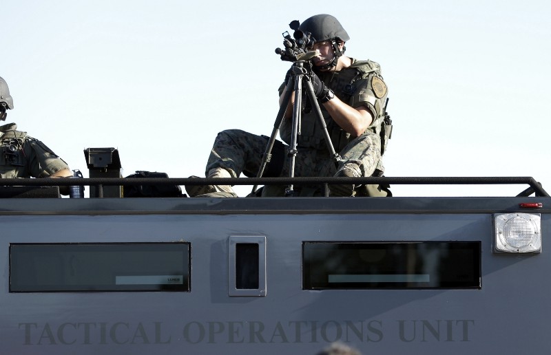 A member of the St. Louis County Police Department points his weapon in the direction of a group of protesters in Ferguson. CREDIT: AP PHOTO/JEFF ROBERSON
