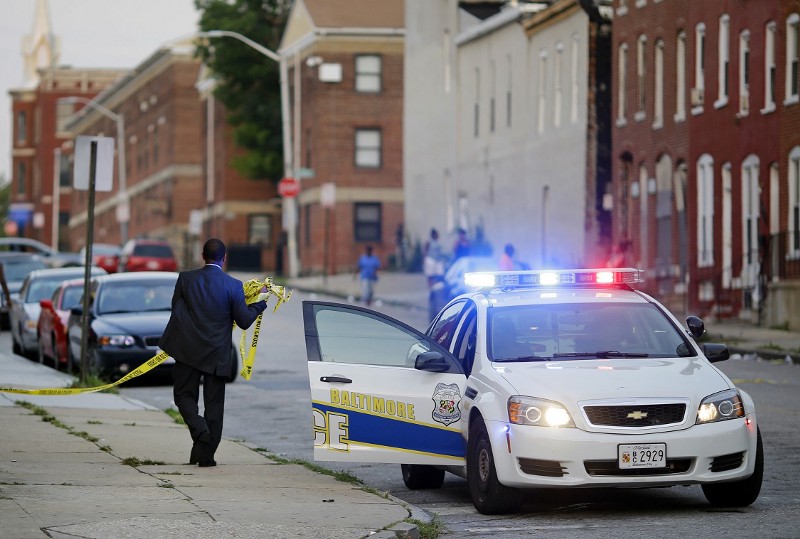 In this July 30, 2015 picture, a member of the Baltimore Police Department removes crime scene tape from a corner where a victim of a shooting was discovered in Baltimore. Murders are spiking again in Baltimore, three months after Freddie Grays death in police custody. CREDIT: PATRICK SEMANSKY, AP
