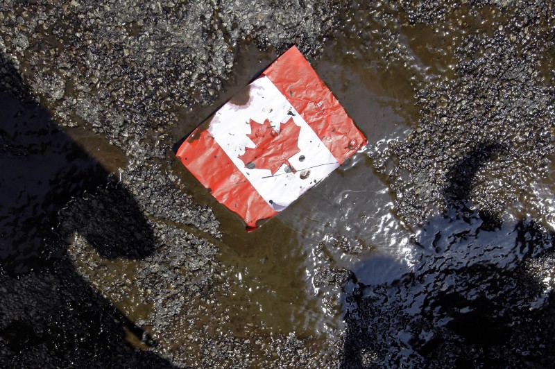 A placard with the Canadian flag rests on the ground covered in oil as demonstrators conduct a die-in to protest against the Keystone Pipeline and the Alberta Tar Sands. CREDIT: AP PHOTO/ NAM Y. HUH