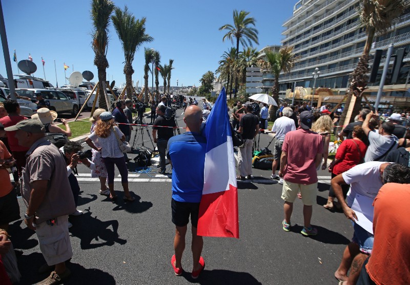 A man holding the French national flag stands near the site of the truck attack in the French resort city of Nice, southern France, Friday, July 15, 2016. CREDIT: AP PHOTO/LUCA BRUNO