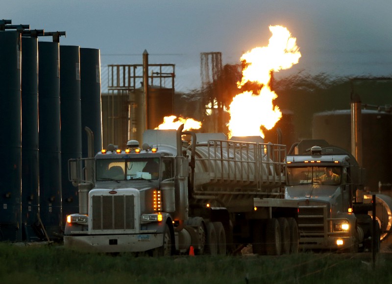 Drivers and their tanker trucks, capable of hauling water and hydraulic fracturing liquid, line up near a natural gas burn off flame and storage tanks in Williston, N.D. CREDIT: AP PHOTO/CHARLES REX ARBOGAST