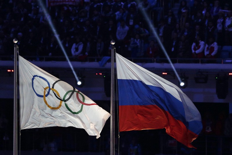 FILE — In this Feb. 23, 2014 file photo the Russian national flag, right, flies after it is hoisted next to the Olympic flag during the closing ceremony of the 2014 Winter Olympics in Sochi, Russia. On Monday, July 18, 2016 a report on Russian doping by investigator Richard McLaren is to be released in Toronto. CREDIT: MATHTIAS SCHRADER, AP