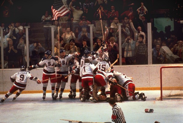 The 1980 U.S. hockey team pounces on goalie Jim Craig after a 4–3 victory against the Soviets in the 1980 Olympics, as a flag waves from the partisan Lake Placid, N.Y. crowd. This victory is colloquially known as the “Miracle On Ice” CREDIT: AP PHOTO/FILE