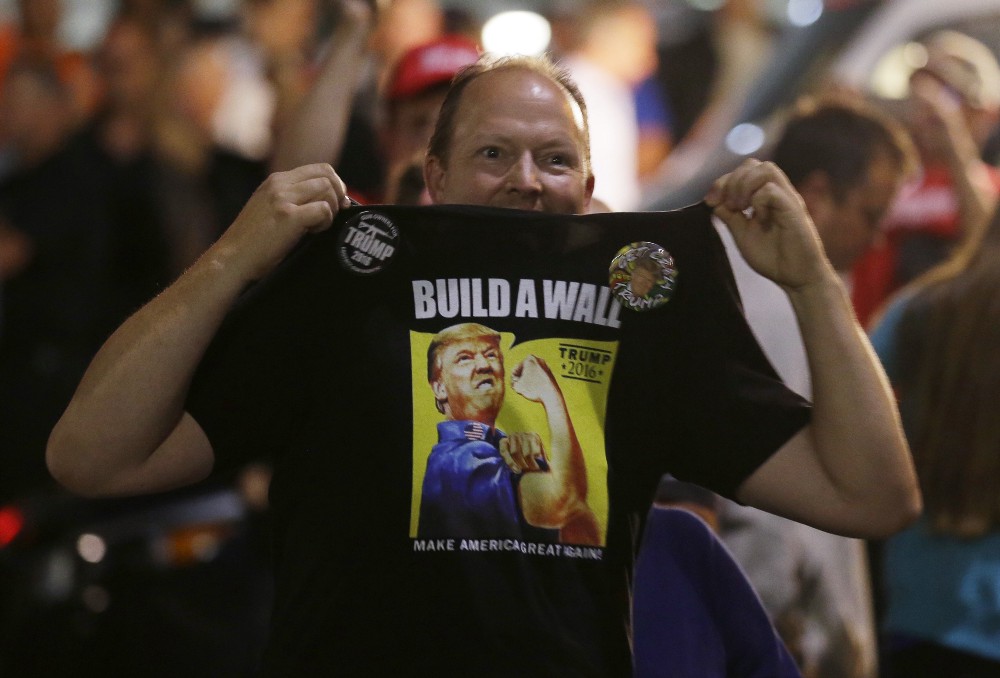 A supporter of Republican presidential candidate Donald Trump holds up his shirt, with the slogan “Build a Wall,” following a Trump rally, Aug. 30, 2016, in Everett, Wash. CREDIT: AP Photo/Ted S. Warren