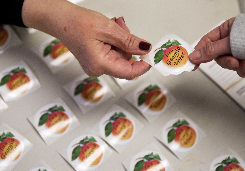 Poll worker Delores Peterson, left, hands a sticker to a voter after they cast their ballot in Georgia’s primary election at a polling site in Atlanta. CREDIT: AP Photo/David Goldman