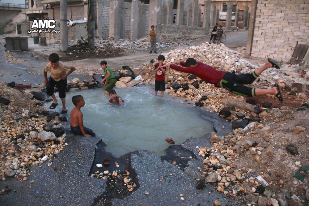 Syrian boys dive into a hole filled with water that was caused by a missile attack in the rebel-held neighborhood of Sheikh Saeed in Aleppo province, Syria, Aug. 13. 2016. CREDIT: ALEPPO MEDIA CENTER/AP