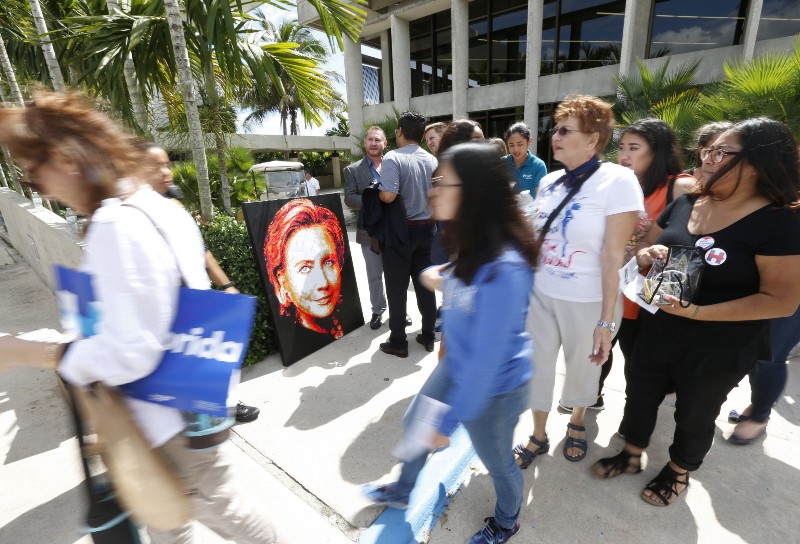 Attendees walk past a portrait of Democratic presidential candidate Hillary Clinton as they arrive for a rally in Miami, Tuesday, Oct. 11, 2016. CREDIT: AP Photo/Wilfredo Lee
