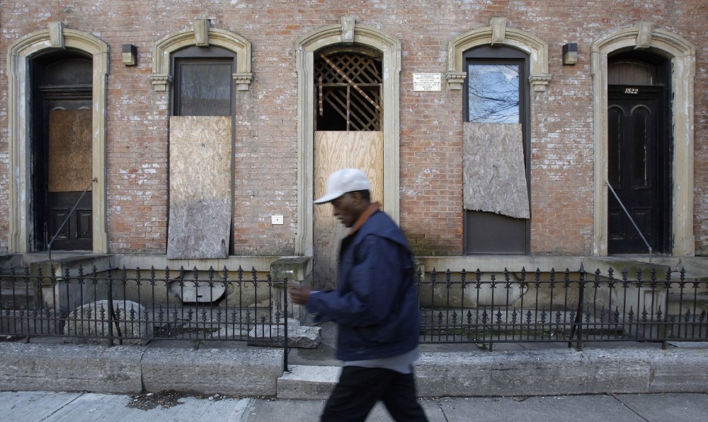 A man walks past a boarded-up building in Cincinnati. CREDIT: AP Photo/Al Behrman