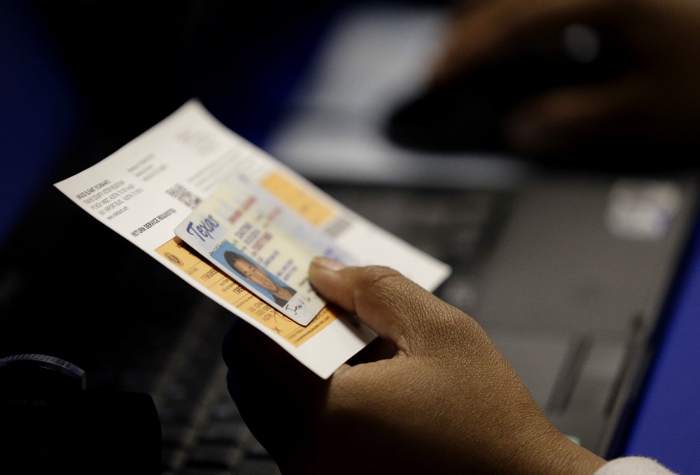 In this Feb. 26, 2014 file photo, an election official checks a voter’s photo identification at an early voting polling site in Austin, Texas. In August 2016, a judge softened the states stringent voter ID law, but early reports and polling show that most people in Texas are confused about the requirements. CREDIT: AP Photo/Eric Gay, File