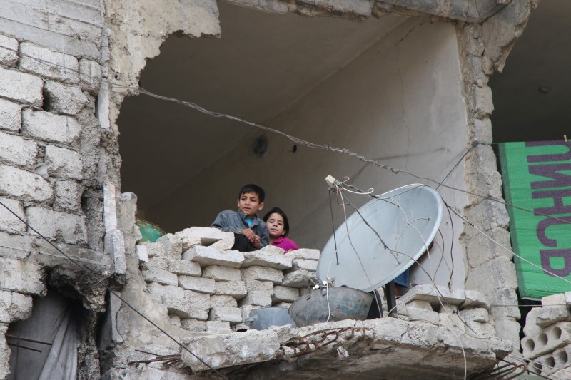 In this Feb. 11, 2016, file photo, children peer from a partially destroyed home in Aleppo, Syria. CREDIT: Alexander Kots/Komsomolskaya Pravda via AP