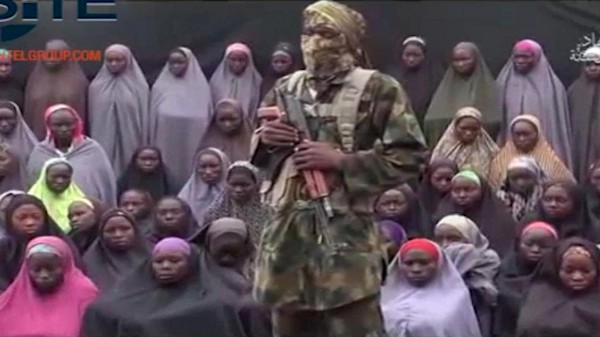 In this undated image taken from video distributed Sunday, Aug. 14, 2016, an alleged Boko Haram soldier standing in front of a group of girls alleged to be some of the 276 abducted Chibok schoolgirls held since April 2014, in an unknown location. CREDIT: Militant video/Site Institute via AP File