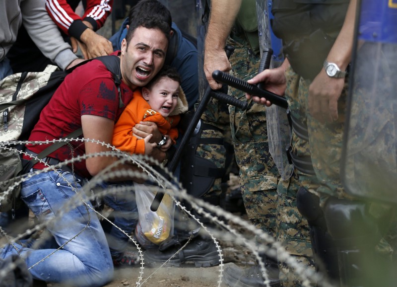 A migrant man and a boy react as they are stuck between Macedonian riot police officers and migrants during a clash near the border train station of Idomeni, northern Greece. AP Photo/Darko Vojinovic, File)