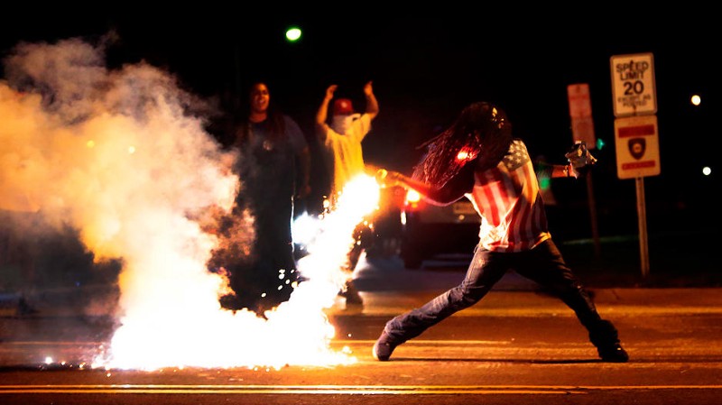 Edward Crawford throws back a tear gas container after tactical officers worked to break up a group of bystanders on Chambers Road and West Florissant on Wednesday, Aug. 13, 2014 in St. Louis. CREDIT: AP Photo/St. Louis Post-Dispatch/Robert Cohen