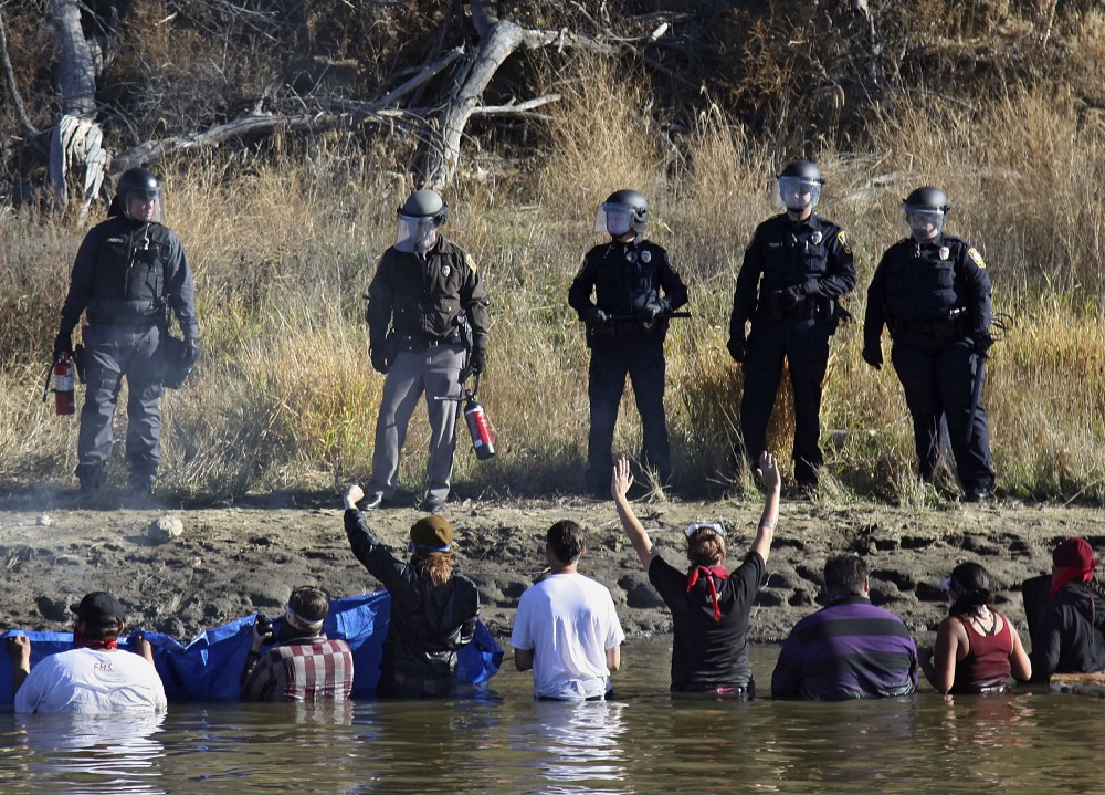 Dozens of protestors demonstrating against the expansion of the Dakota Access Pipeline wade in cold creek waters confronting local police. CREDIT: AP Photo/John L. Mone