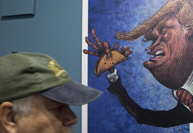An American visitor walks past a cartoon of a Mexican wrapped in a taco sticking his tongue out at a depiction of President-Donald Trump, in an exhibition titled; “Trump: A wall of caricatures,” at the Caricature Museum in downtown Mexico City CREDIT: AP Photo/Rebecca Blackwell