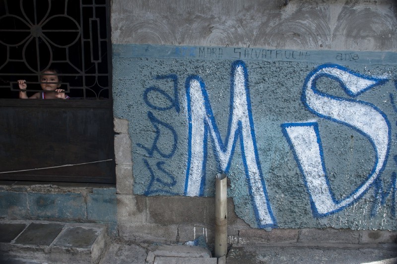 In this June 21, 2016 photo, a child peers from behind the door of her home, covered with Mara Salvatrucha gang graffiti, in Soyapango, El Salvador. CREDIT: P Photo/Salvador Melendez