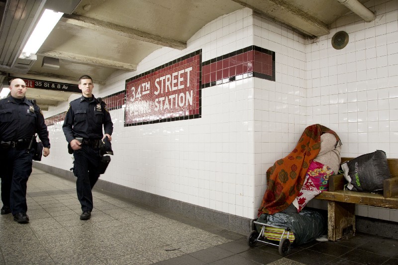 NYPD officers pass a homeless woman while patrolling the subway system in 2014. CREDIT: AP Photo/Mark Lennihan