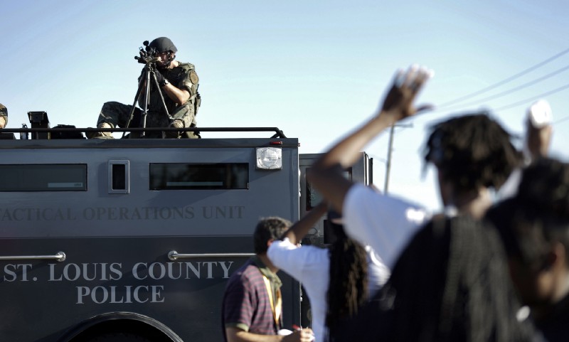 A member of the St. Louis County Police Department points his weapon in the direction of a group of protesters in Ferguson, MO. CREDIT: AP Photo/Jeff Roberson