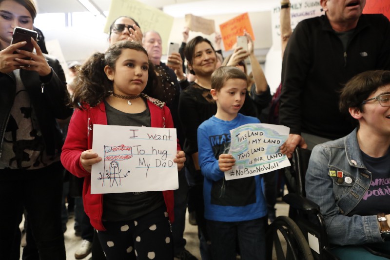 Seven-year-old Teyom Karimi, left, holds a sign as protests against President Donald Trump’s executive order banning travel from seven Muslim-majority countries continue at Los Angeles International Airport Sunday, Jan. 29, 2017. CREDIT: AP Photo/Ryan Kang