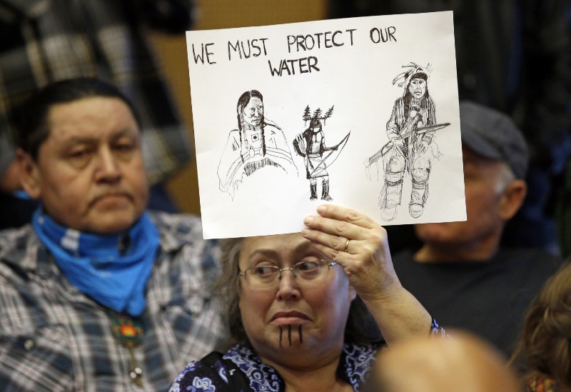 Lisa Anderson, a member of the Chumash-Ohlone tribe, holds a sign favoring divestment before a Seattle City Council meeting Tuesday, Feb. 7. CREDIT: AP Photo/Elaine Thompson