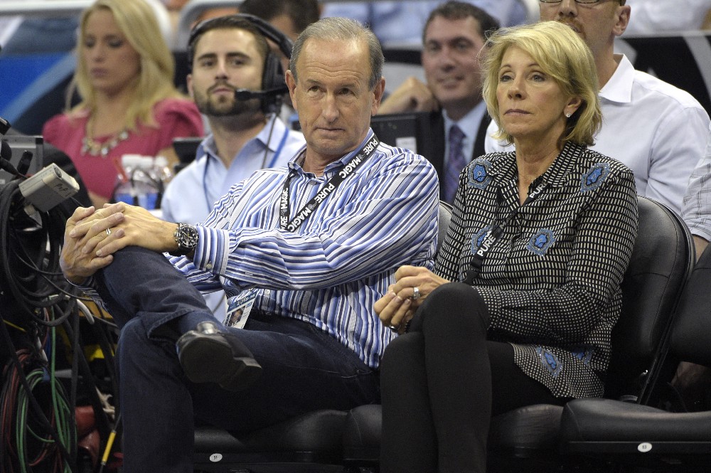Dick DeVos, center, son of Orlando Magic Chairman Rich DeVos, and his wife Betsy DeVos, right, watch from their court side seats during the second half of an NBA basketball game against the Minnesota Timberwolves in Orlando, Fla., Wednesday, Nov. 18, 2015. The Magic won 104–101. CREDIT: AP Photo/Phelan M. Ebenhack