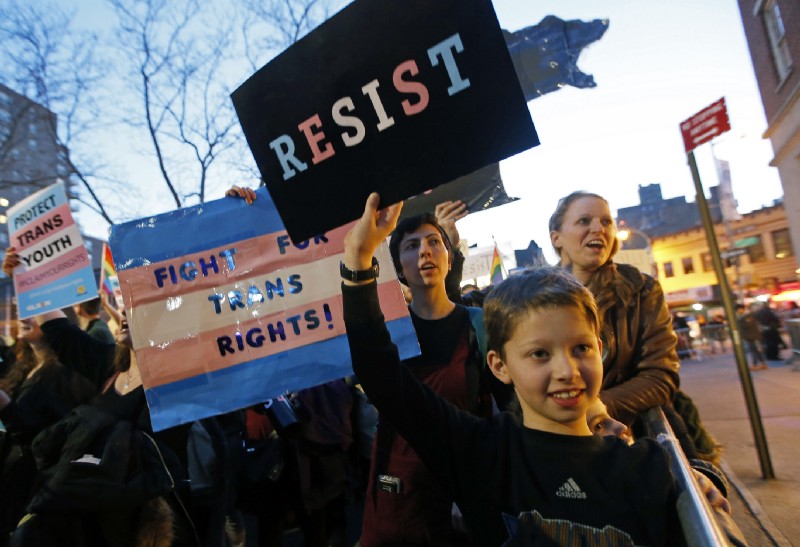 Tal Moskowitz, 8, front, a transgender child, holds a sign as his parents Faigy Gelbstein, left, and Naomi Moskowitz, upper right, of Long Island, hold separate signs during a rally in support of transgender youth at the Stonewall National Monument, Thursday, Feb. 23, 2017, in New York. They were among demonstrators The crowd gathered Thursday night in front of the Stonewall Inn. The family were speaking out against President Donald Trump’s decision to roll back a federal rule saying public schools had to allow transgender students to use the bathrooms and locker rooms of their chosen gender identity. The rule had already been blocked from enforcement, but transgender advocates view the Trump administration action as a step back for transgender rights. CREDIT: AP Photo/Kathy Willens