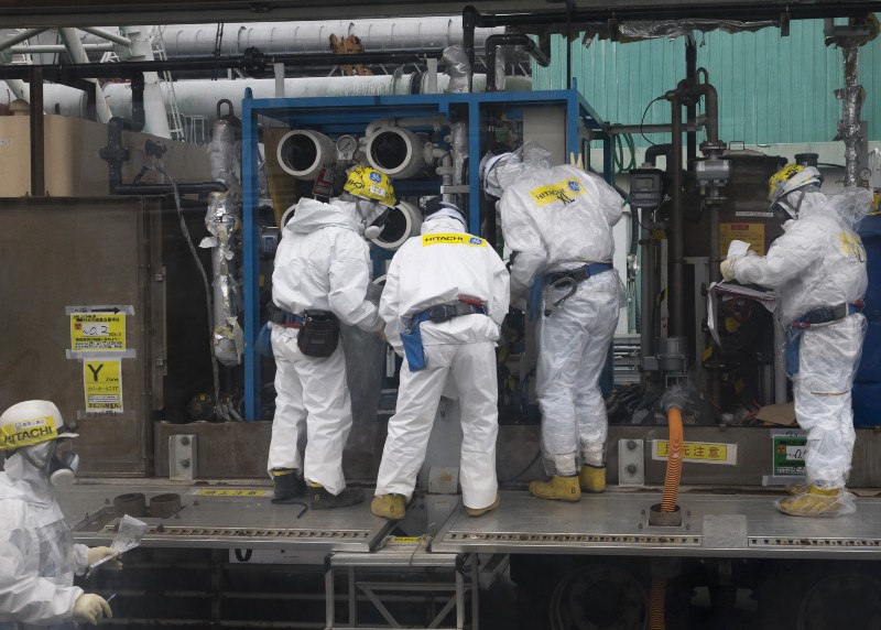 Workers wearing protective gear are seen through a bus window during a media tour to the tsunami-crippled Fukushima Dai-ichi nuclear power plant, Feb. 2017. CREDIT: Tomohiro Ohsumi/Pool Photo via AP
