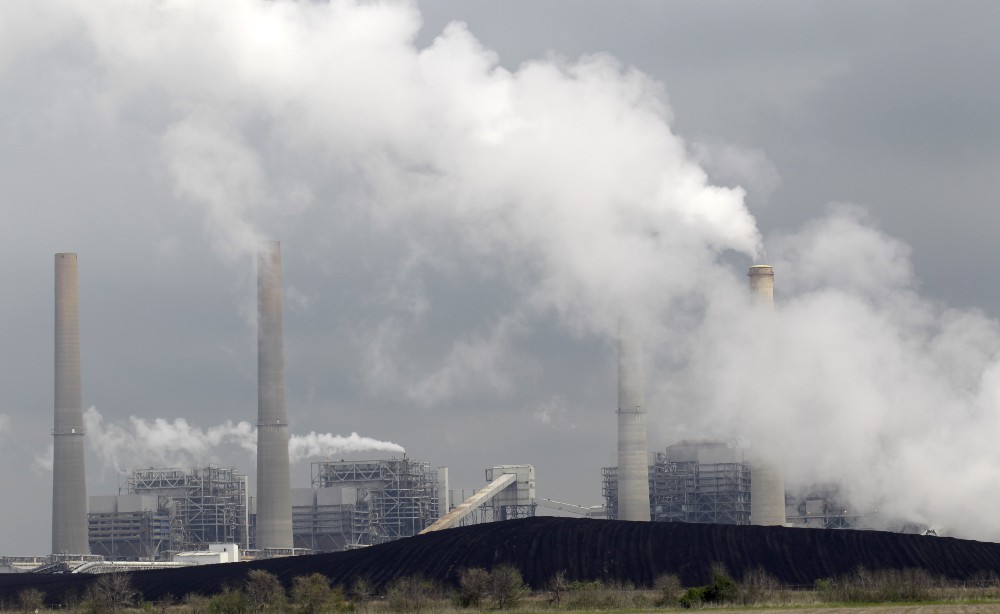 Exhaust rises from smokestacks in front of piles of coal at NRG Energy’s W.A. Parish Electric Generating Station in Thompsons, TX. CREDIT: AP Photo/David J. Phillip