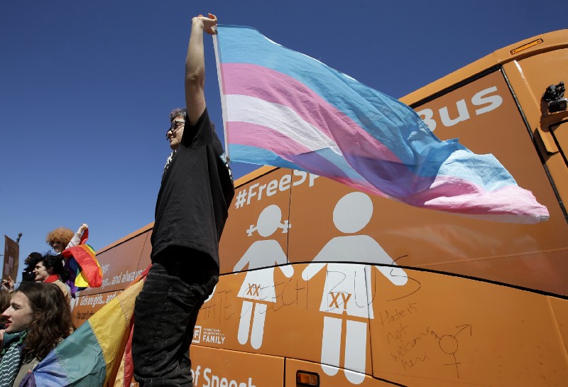 Leon Weiler, of Cambridge, Mass., top, holds a flag while standing with other protesters in support of transgender rights. Credit: AP Photo/Steven Senne)