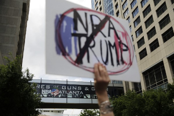 A demonstrator holds a sign during a protest across the street from the National Rifle Association’s annual convention where President Donald Trump is scheduled to speak in Atlanta, Friday, April 28, 2017. CREDIT: AP Photo/David Goldman