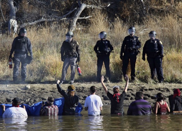 Dozens of protesters demonstrating against the expansion of the Dakota Access Pipeline wade in creek waters confronting local police. CREDIT: AP Photo/John L. Mone