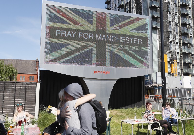 A couple embrace under a billboard in Manchester city centre, Tuesday May 23, 2017, the day after the suicide attack at an Ariana Grande concert that left 22 people dead as it ended on Monday night. CREDIT: AP Photo/Kirsty Wigglesworth