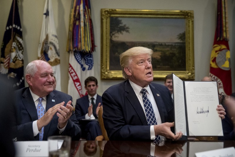 Secretary of Agriculture Sonny Perdue, left, applauds President Donald Trump’s signing of an executive order in April. CREDIT: AP Photo/Andrew Harnik
