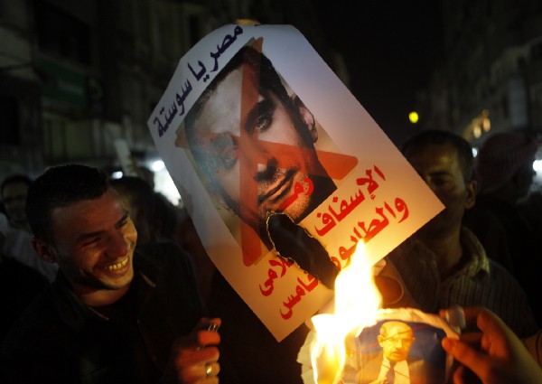 In this Wednesday, Oct. 30, 2013 photo, Supporters of Defense Minister Gen. Abdel-Fattah el-Sissi burn a poster with a photo of Bassem Youssef and Arabic that reads, “not Egypt, you are degrading to the media, fifth column,” during a protest in Cairo, Egypt. Several complaints were filed against Youssef, after he mocked the pro-military fervor gripping Egypt in his first program of the season last week. Youssef also took jabs at the powerful El-Sissi, lionized in the local media after leading a July 3 overthrow that ousted the Islamist president. CREDIT: AP Photo/Amr Nabil)