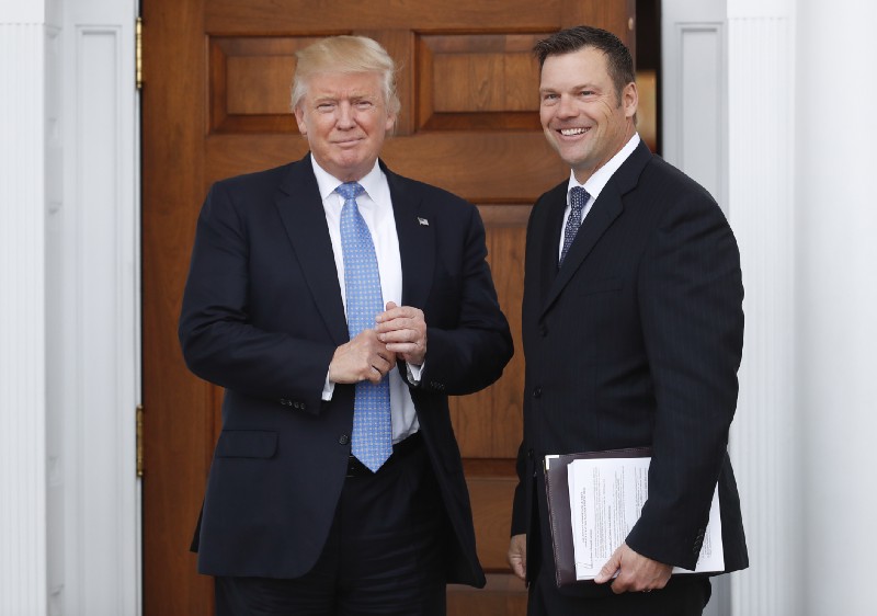 Kansas Secretary of State Kris Kobach, right, carries paperwork as he is greeted before a meeting with then President-elect Donald Trump at the Trump National Golf Club Bedminster clubhouse in Bedminster, N.J. CREDIT: AP Photo/Carolyn Kaster, File