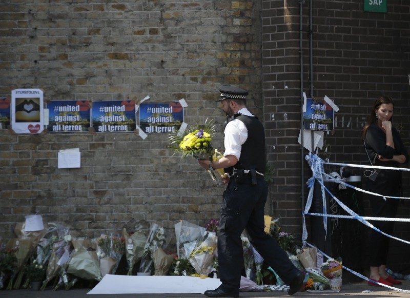 A policeman carries flowers left by a well-wisher after a driver plowed into a crowd of people leaving a mosque early Monday morning. CREDIT: AP/Alastair Grant