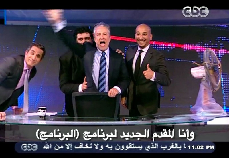 Jon Stewart talks to the studio audience in Cairo, Egypt, Friday June 21, 2013, on Egypt’s top satirical TV program modeled after his own program “The Daily Show”. Stewart was introduced by Egyptian TV host Bassem Youssef, left, wearing a black hood as a captured spy for the program, and the hood was dramatically lifted off before continuing the show. CREDIT: AP Photo / CBC