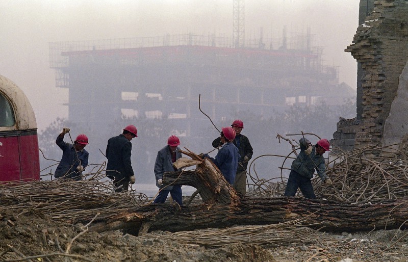 Chinese workers collect reinforcing steel from a demolition site in Beijing. Looming behind them in the smog is one of many construction sites in the heart of Beijing’s shopping district. CREDIT: AP Photo/Greg Baker