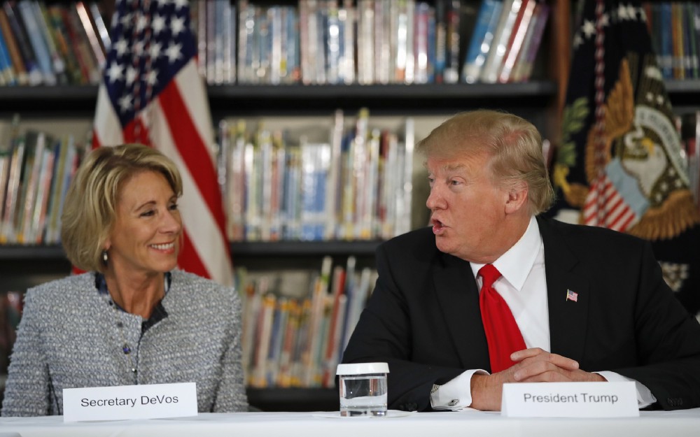 Education Secretary Betsy DeVos listens at left as President Donald Trump speaks during a round table discussion at Saint Andrew Catholic School, Friday, March 3, 2017, in Orlando, Fla. CREDIT: AP Photo/Alex Brandon