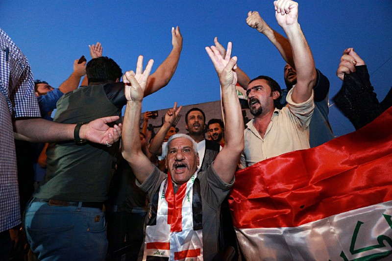 Iraqis celebrate in Tahrir square while holding national flags as they wait for the final announcement of the defeat of the Islamic state, in Baghdad, Iraq, July 9, 2017. CREDIT: AP Photo/Hadi Mizban