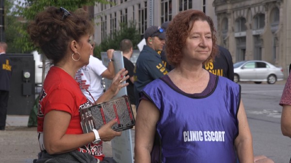 A clinic escort stands along the buffer zone as a protester prays over her. CREDIT: Katelyn Marmon