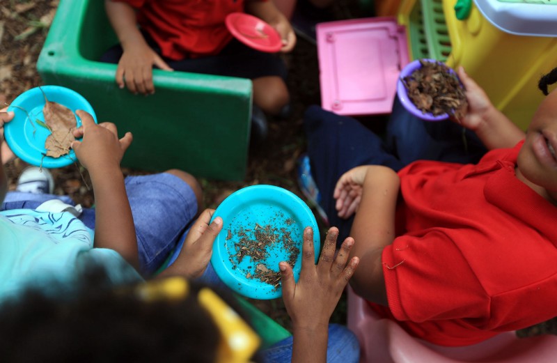 The children in this New Orleans child care center scoop piles of dirt and leaves onto plates in their play kitchen in the backyard where Tulane University’s School of Medicine Professor Howard Mielke had a contractor cover the existing soil with geotextile fabric and a six-inch clean soil cap atop the fabric. CREDIT: Daniel A. Anderson for ThinkProgress